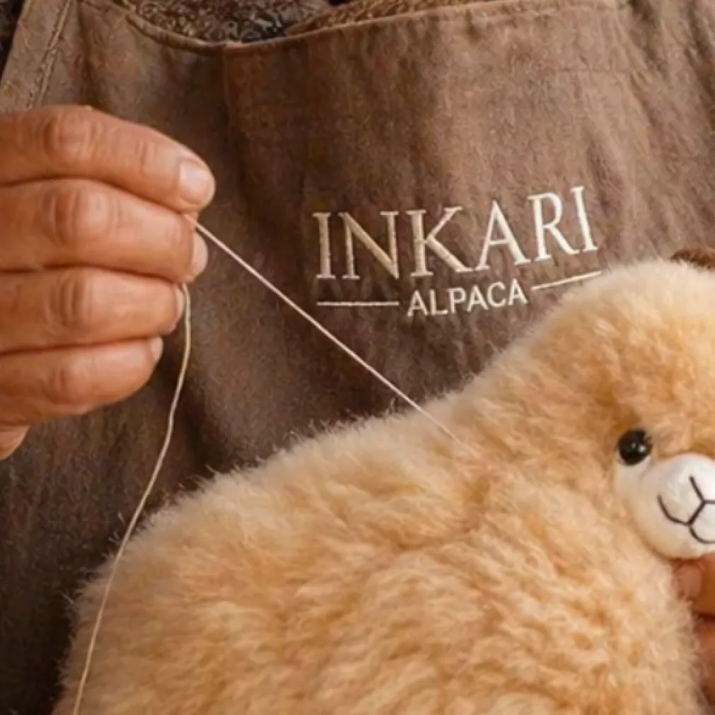 An artisan stitching the Inkari label onto a plush alpaca by hand